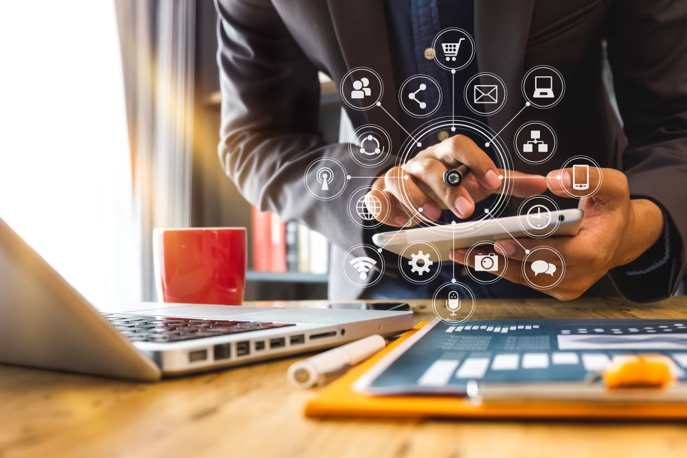 Business professional using a tablet beside a laptop with overlaid digital connectivity and e‑commerce icons