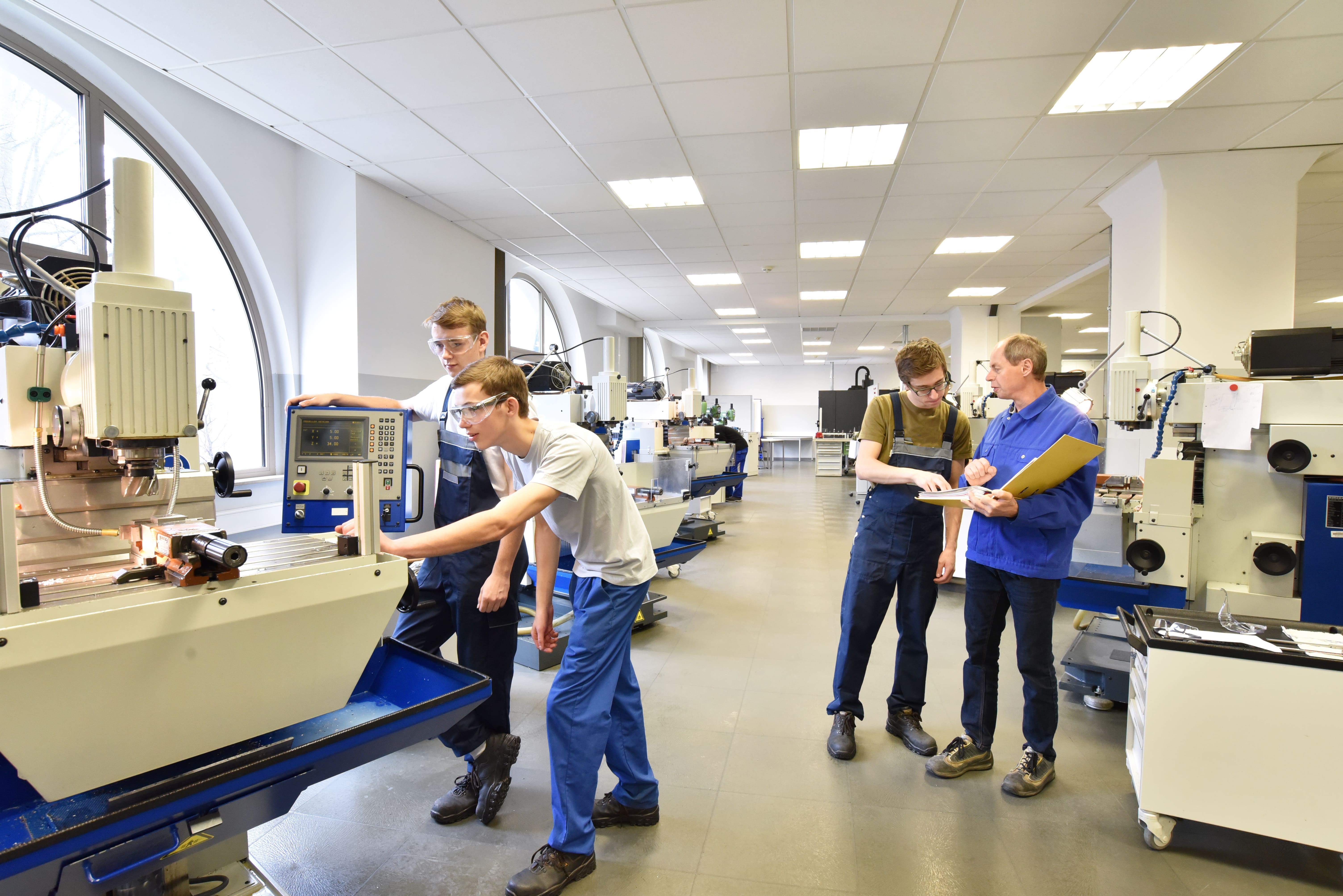 Apprentice machinists operating CNC milling machines under instructor guidance in a modern workshop
