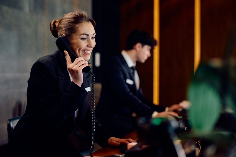 Happy hotel manager talking on phone at reception desk