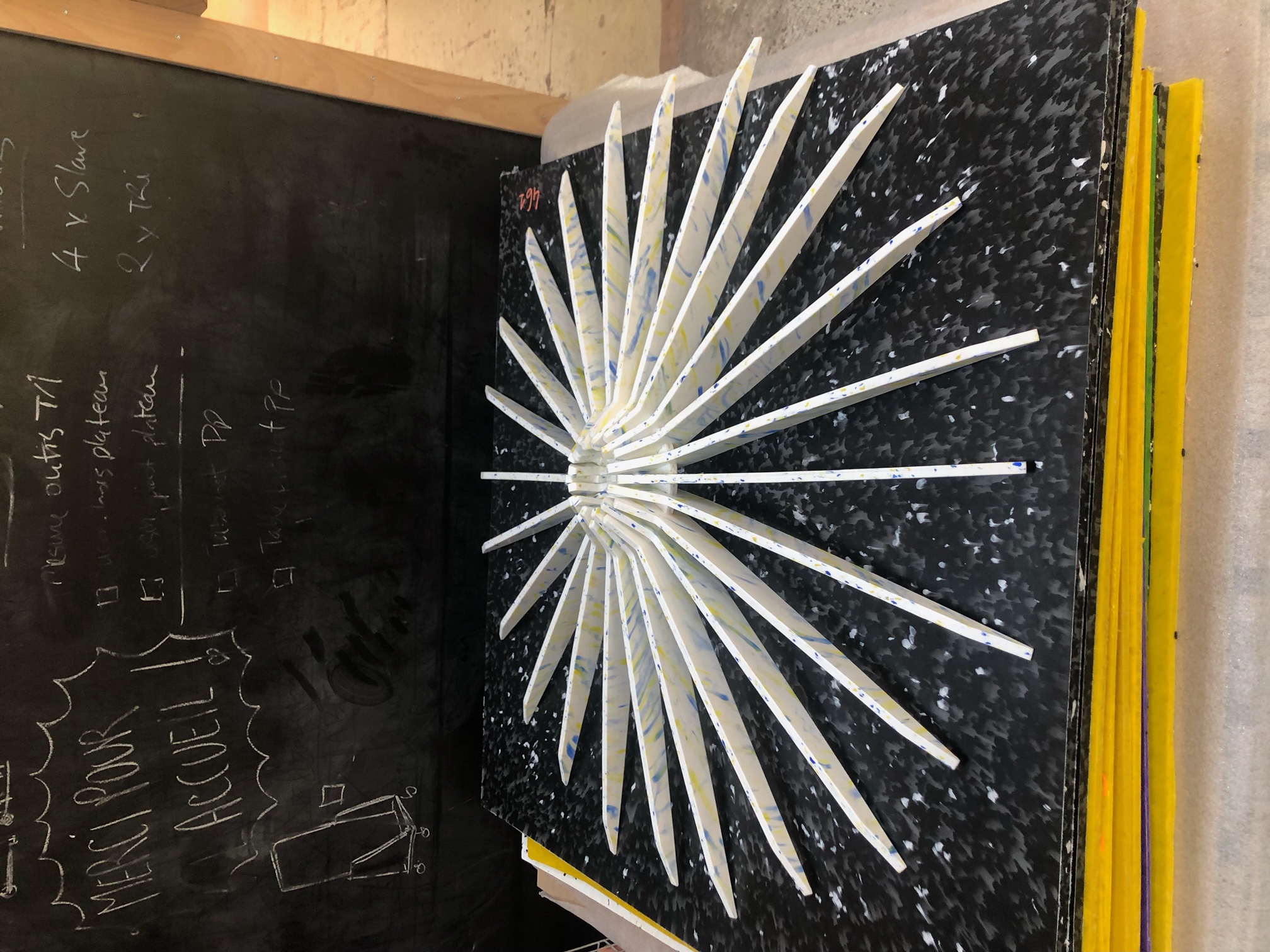 Sculpture abstraite en atelier, composition radiale de lames peintes blanches, bleues et jaunes disposées en étoile sur un support noir